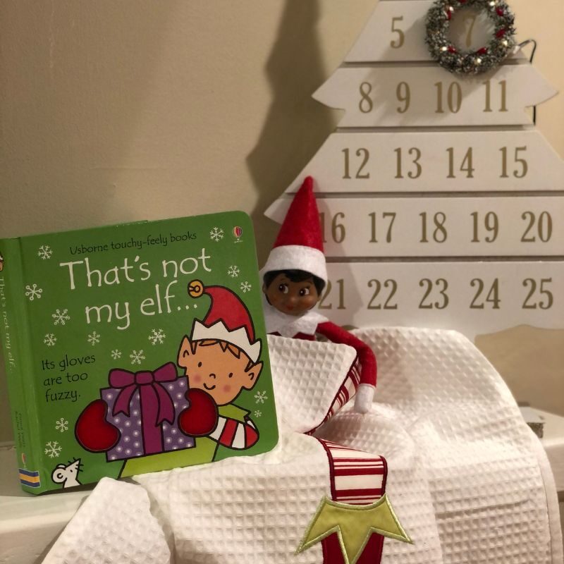 An Elf on the Shelf sits with a book they "brought" from the North Pole. 